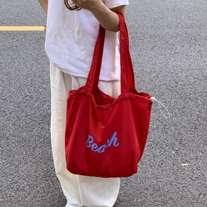 Detail of red drawstring tote bag with blue Beach lettering held by a model