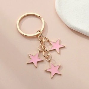 Detail of three light pink enamel star charms on a gold keychain with flat lay aesthetic