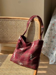 Détail du sac en tissu écossais rouge avec nœuds brodés blancs sur une chaise en rotin