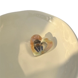 Elegant heart-shaped hollow acetate hair clip with amber marble texture in a ceramic bowl
