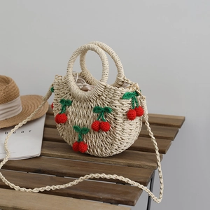 Handgefertigte beige Strohtasche mit Häkelkirschen auf einer rustikalen Holzbank