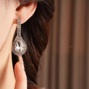Close-up of teardrop diamond earrings worn by model with professional focus and soft lighting