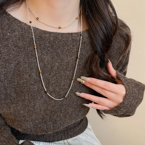 Detail of beaded necklace with tiger eye and white beads on a brown sweater