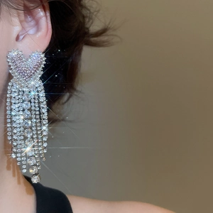 Close-up of heart-shaped earrings with long rhinestone tassels worn by a model