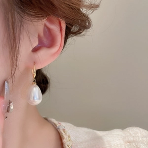 Close-up of a model wearing elegant white teardrop pearl earrings with gold hooks