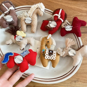 Detailed view of handmade fabric horse brooches in various colors displayed on a ceramic plate