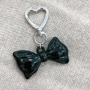 Detail of glossy black acrylic bow keychain with silver heart clasp on gray knit background