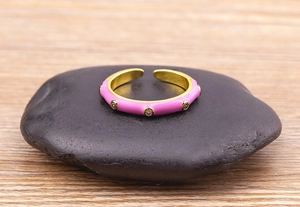 Detail of pink enamel gold ring with zircon stones on a black pebble background