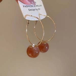 Detail of amber resin ball pendant on a golden hoop earring against a jewelry card