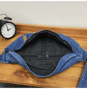 Detailed view of the open denim crossbody bag showing black lining and interior zipper pocket