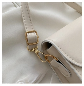 Detail of adjustable strap with gold-tone hardware on a cream-colored saddle bag