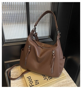 Close-up of vintage brown PU leather shoulder bag with side zippers on a decorative book