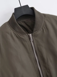 Detailed close-up of military green bomber jacket featuring ribbed collar and silver zipper