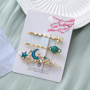 Star and moon gold metal hair clips with blue planet and pearls on a floral card