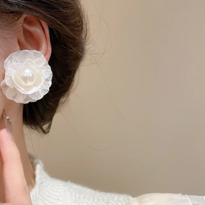 Close-up of elegant cream fabric flower earrings with a centered lustrous pearl