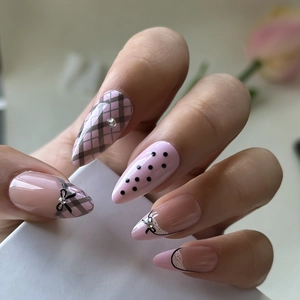 Nahaufnahme rosa Mandel-Kunstnägel mit schwarzen Schleifen, Karomuster und Strasssteinen
