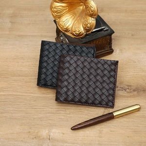 Classic men's woven leather bifold wallet in black and dark brown on a wooden desk