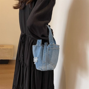 Close-up of light blue denim bucket bag with distressed pocket and topstitched details