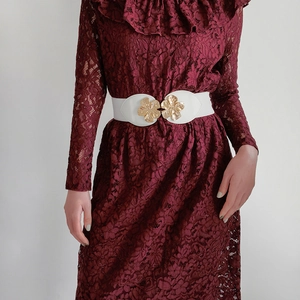 Detail of white elastic waist belt with gold peach blossom buckle on a red dress