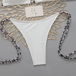 Flat lay of white high-waisted bikini bottoms with leopard print side ties and golden props