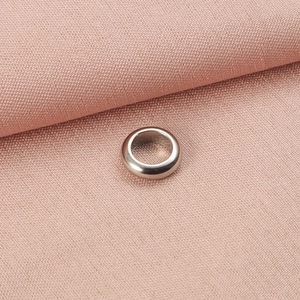 Macro shot of silver stainless steel spacer bead on a pink textured fabric background