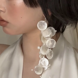 Elegant drop earrings with white shell discs and pearls worn by a model in soft light