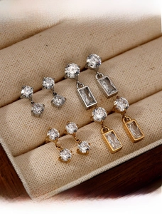 Close-up of elegant gold and silver zircon earrings displayed in a beige jewelry box