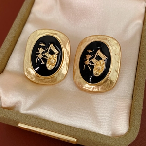 Detailed close-up of vintage gold oval earrings with black enamel and carriage relief