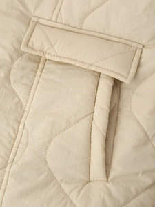 Close-up of diamond quilted texture and flap pocket detail on beige jacket