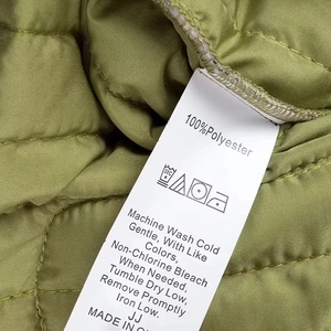 Detail of care label on olive green quilted jacket showing material and washing instructions