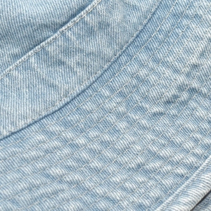 Detailed close-up of light blue denim fabric with parallel stitching on sun hat brim