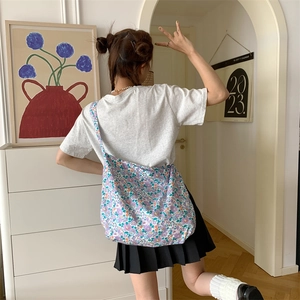 Detail view of a large purple floral canvas tote bag worn by a model in a cozy interior