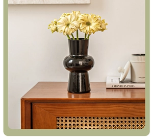 Detail of a vintage black glass vase with yellow flowers on a wooden cabinet