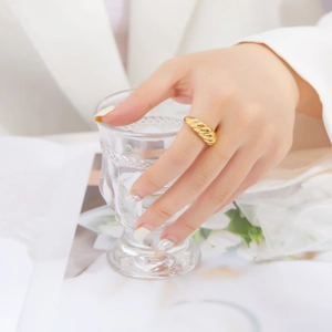 Close-up of golden croissant dome ring with twisted texture worn on hand with glass