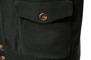 Macro shot of dark green knit fabric texture with brown amber button and pocket detail