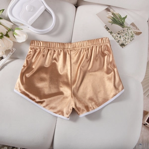 Detailed view of gold satin athletic shorts with white trim laid on a soft sofa