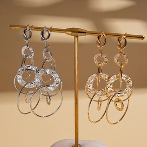 Layered geometric metal hoop earrings in gold and silver finish on a display stand