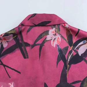 Dettaglio del colletto di una camicia in raso rosa con stampa floreale e foglie nere