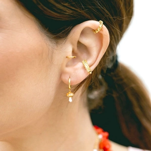 Close-up of golden mushroom earrings and enamel ear cuffs worn on female ear model