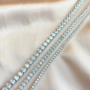 Detailed macro shot of four sparkling S925 silver tennis bracelets on beige silk fabric