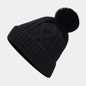 Close-up of black cable knit beanie featuring a large faux fur pompom and ribbed cuff