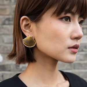 Close-up of golden shell earring with inlaid sparkling white rhinestones on ear
