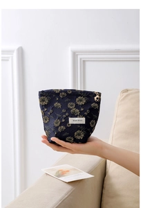 Detail of navy blue fabric makeup bag with gold daisy pattern held in one hand