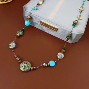 Detail of beaded necklace featuring turquoise accents, a butterfly charm, and textured pendant