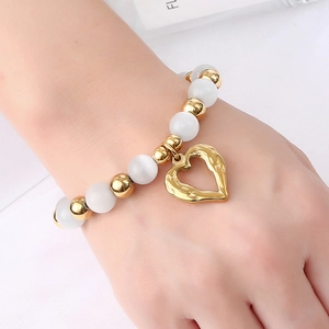 Detail of beaded bracelet with white cat-eye stones and golden hollow heart charm