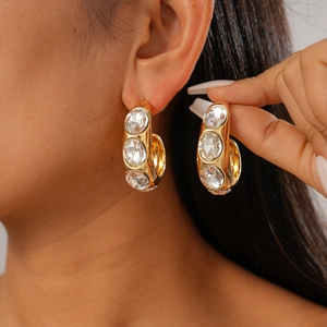 Detail of gold C-shaped hoop earrings with three large transparent gemstones on model
