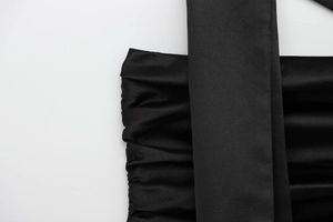 Macro detail of the elegant pleated design on the black satin fabric of the top