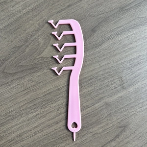 Pink Z-shaped hair comb for volume and styling on dark wood background