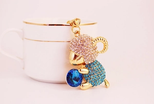 Detail of a golden sheep keychain with sparkling blue and pink crystals on light pink background