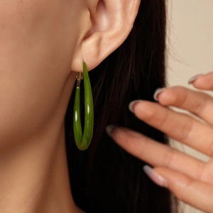 Primo piano di una modella che indossa orecchini a U in resina verde con finitura lucida